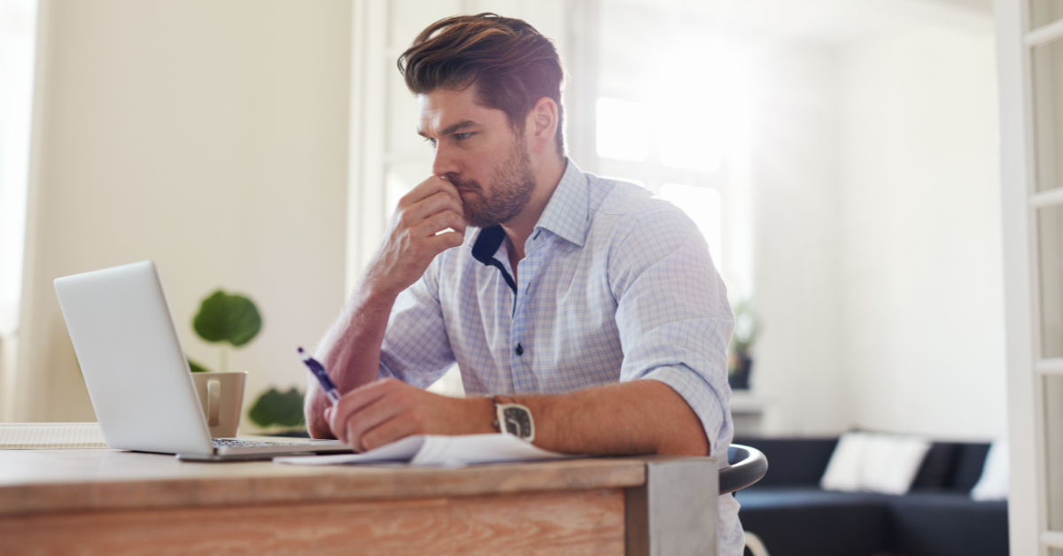A man thinking and contemplating; sitting in front of a computer at a desk.